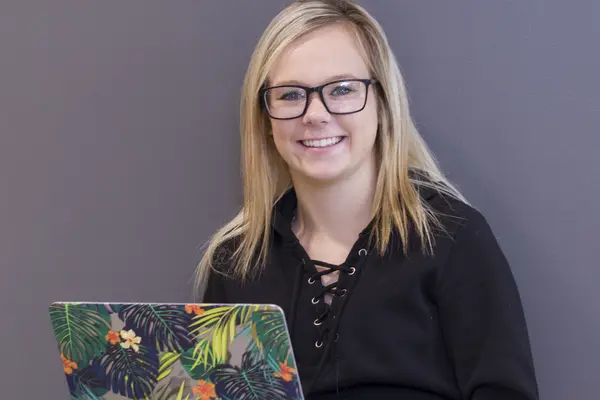Smiling person with glasses using a laptop with a colorful floral cover.