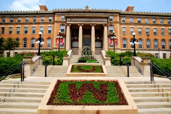 Brick UW Madison building with columns, stairs, and landscaped "U" and "W" in plants.