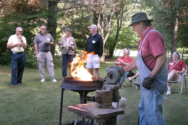 Man demonstrating blacksmithing outdoors to small group at Learning in Retirement event.