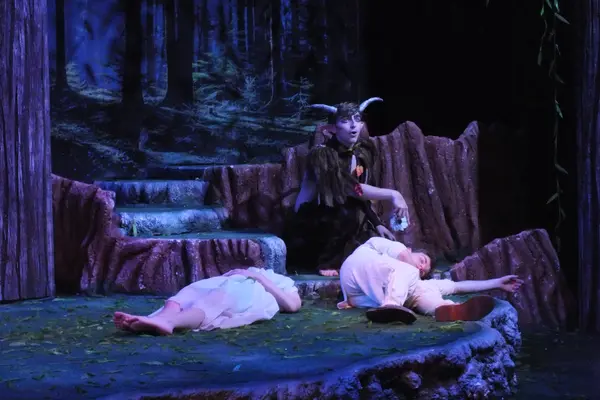 The Nicolet Players performing A Midsummer Night's Dream, forest background and costumed actors lying on stage.