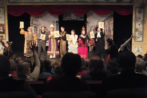 The Nicolet Players performing Edwin Drood. Actors in period costumes holding signs.