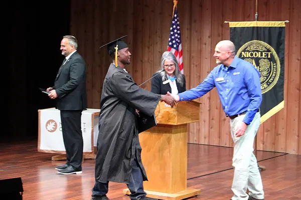 graduate walks across stage and shakes hand with instructor