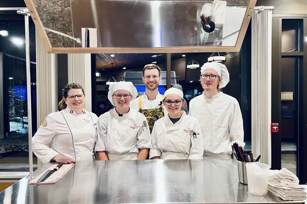 group of student chefs and instructors standing behind a prep table