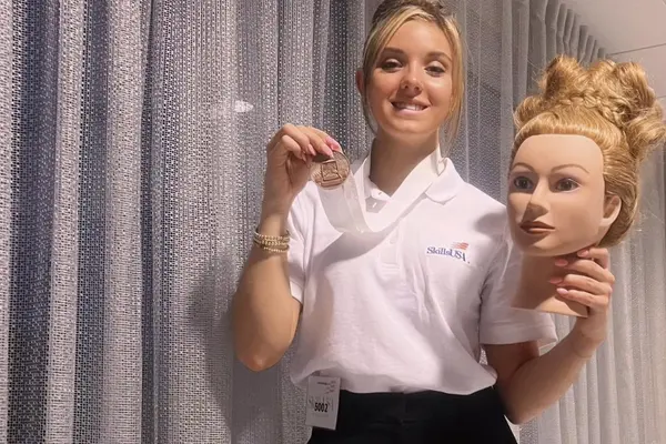 Rachael Reilly, a cosmetology student, holding her bronze medal and mannequin head with an elegant up-do.