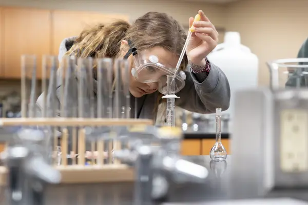 Student in a lab using a dropper with goggles on.