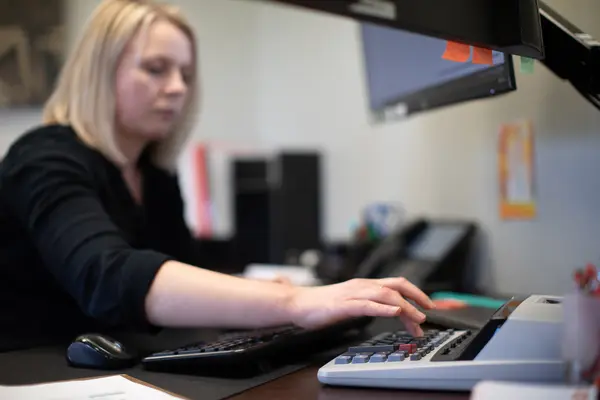 Female accounting student working at a desk with a calculator and monitors.