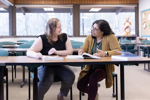 Instructor and student talking through an issue at a table in a classroom