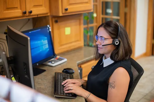 A woman with a headset works at a computer in an office setting.