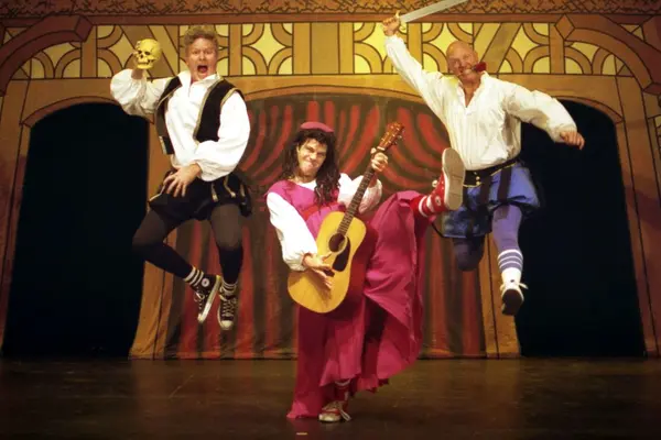 A group of actors on stage in Shakespearean costumes. Two are jumping. 