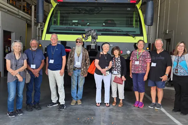 Group of senior citizens posing in a line in front of a large airport truck.