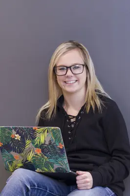 Smiling person with glasses using a laptop with a colorful floral cover.