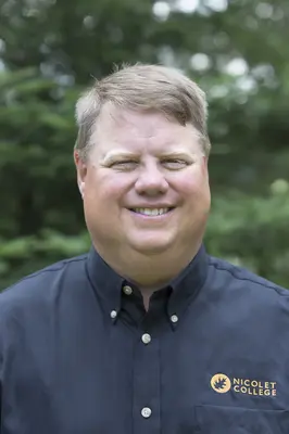 Smiling man in a dark shirt outside with trees in background.