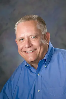 Jim Burst, Nicolet College Foundation Vice President & Treasurer smiling in a blue shirt against a gray background.