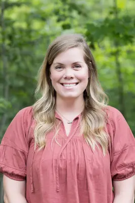 Smiling woman in a forest setting with a peach top.