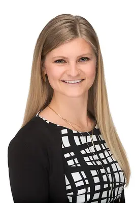 Smiling woman with long blonde hair, wearing a black and white patterned blouse.