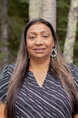 Woman smiling in a forest setting, wearing a striped top and hoop earrings.