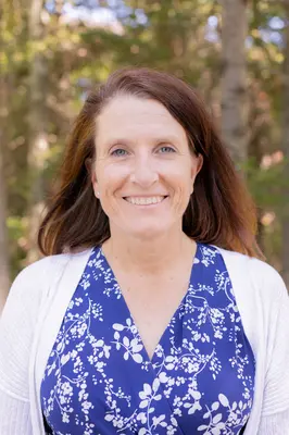 Smiling woman in blue floral dress and white cardigan, outdoors.