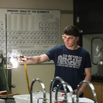 Student conducting science experiment with a Bunsen burner in a lab classroom.