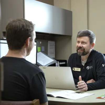 Admissions Representative and student conversing at a desk with a laptop, in a well-lit office.