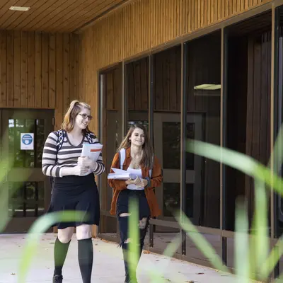 two young female students walking on the sidewalk by a building