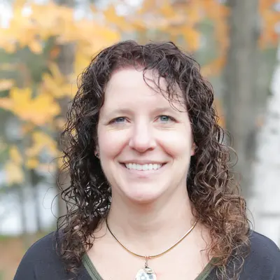 Smiling woman outdoors with autumn leaves in background.