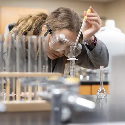 Student in a lab using a dropper with goggles on.