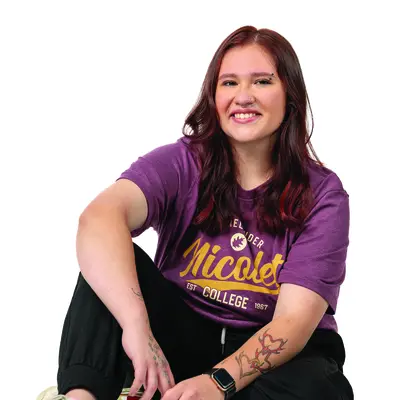 Smiling person seated, wearing a purple shirt and colorful sneakers.