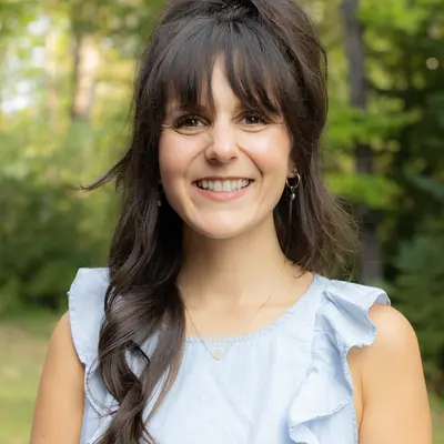 Smiling woman outdoors with a blurred forest background.