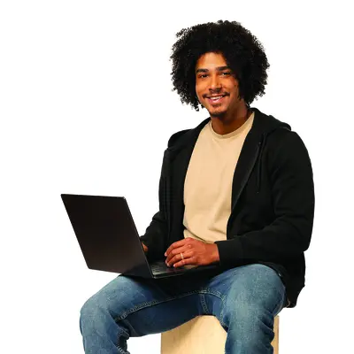 Smiling person sitting with laptop on a stool, wearing casual clothes.