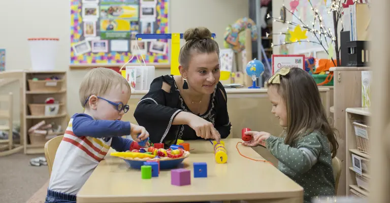 young boy and girl playing at daycare table with student teacher