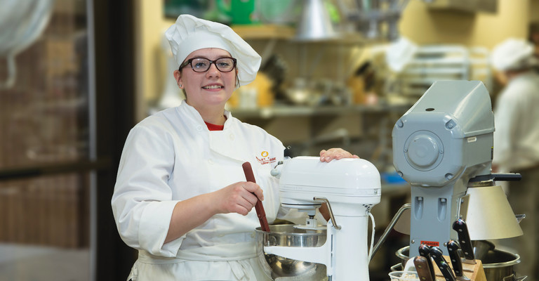 female in chef hat standing next to mixer