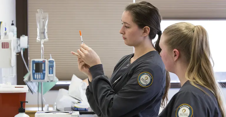 Two nursing students preparing a syringe in a medical setting.