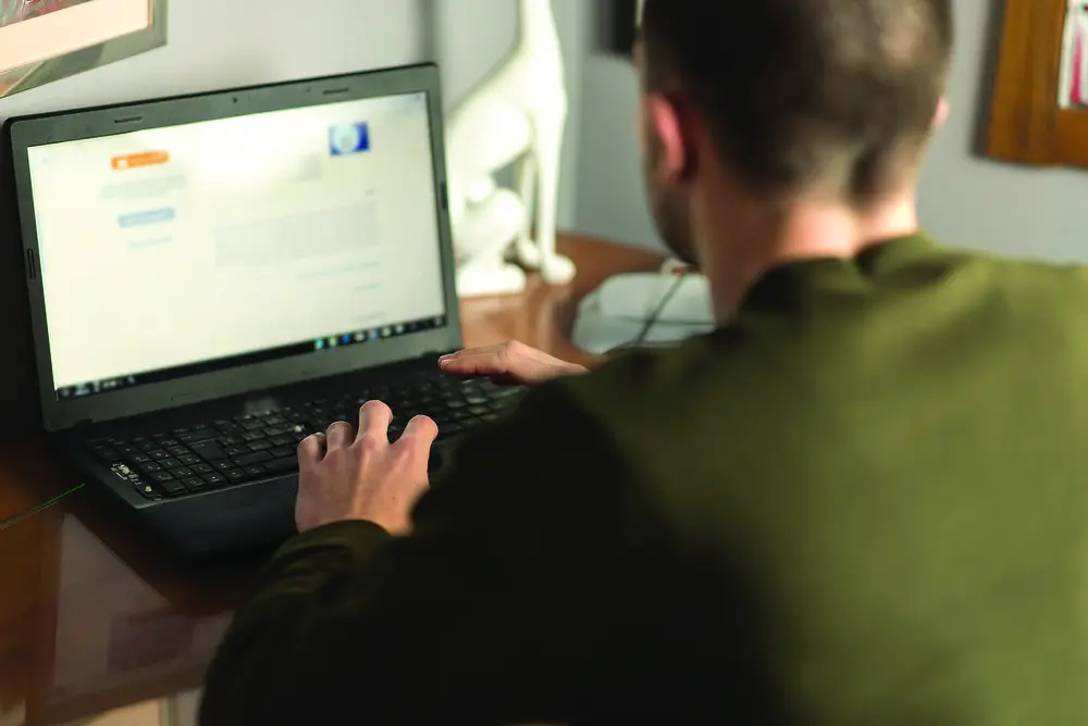 Male Web Developer typing on a laptop at a wooden desk.