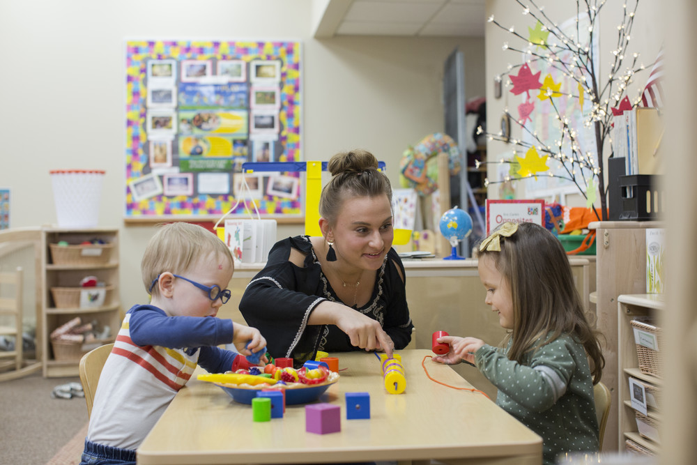 young boy and girl playing at daycare table with student teacher