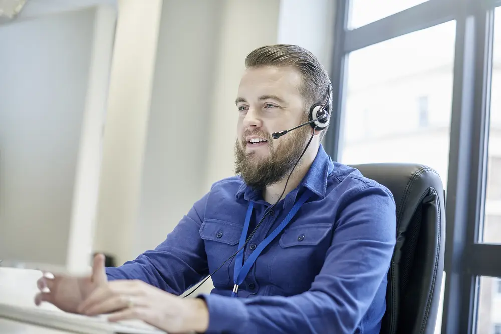 IT user support technician with headset smiling in a bright office setting.
