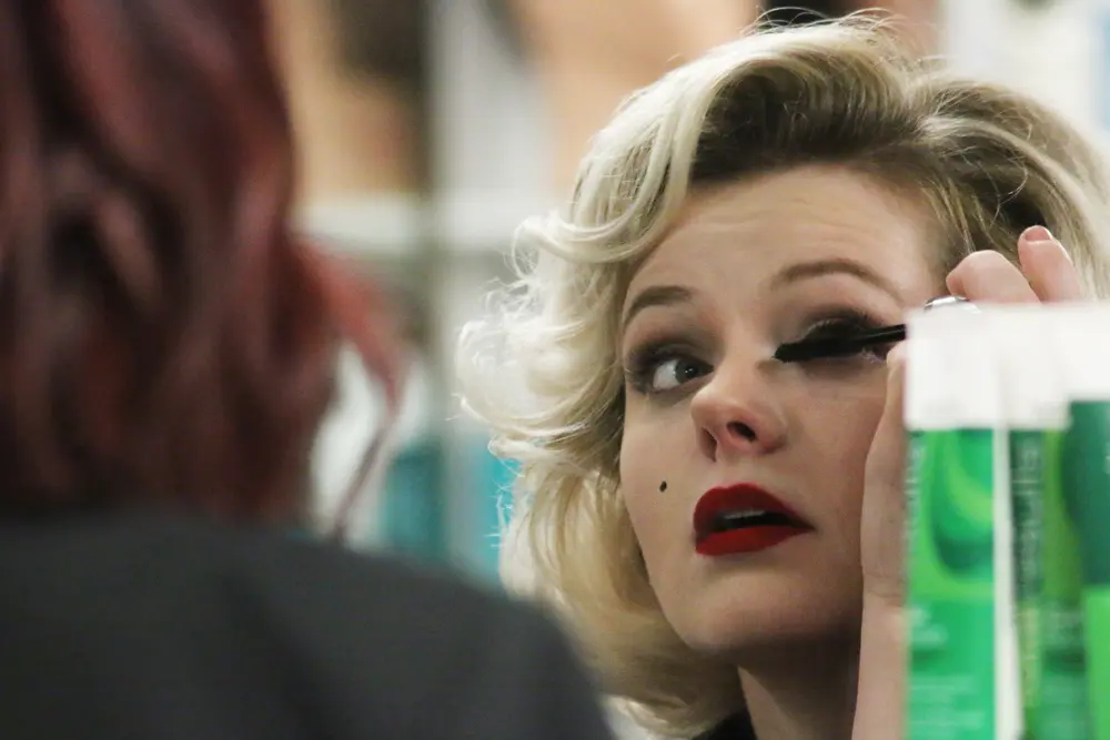 Female Cosmetology student applying mascara to herself in mirror.