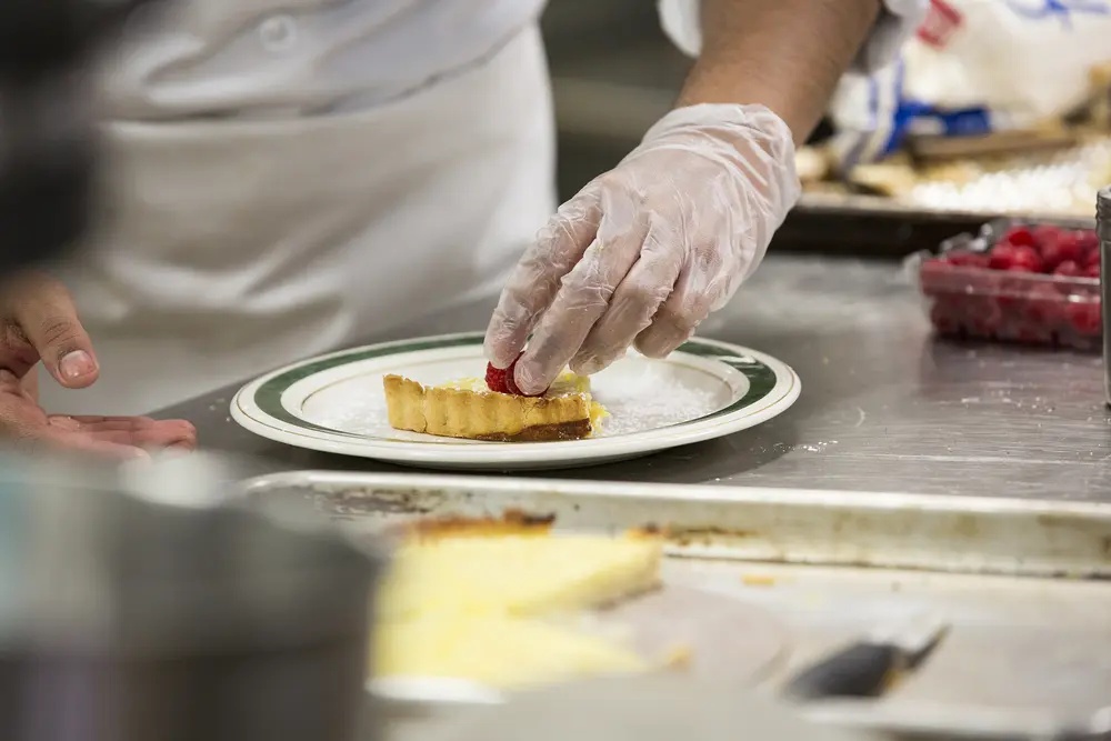 Culinary student placing a raspberry on a dessert plate in a kitchen.