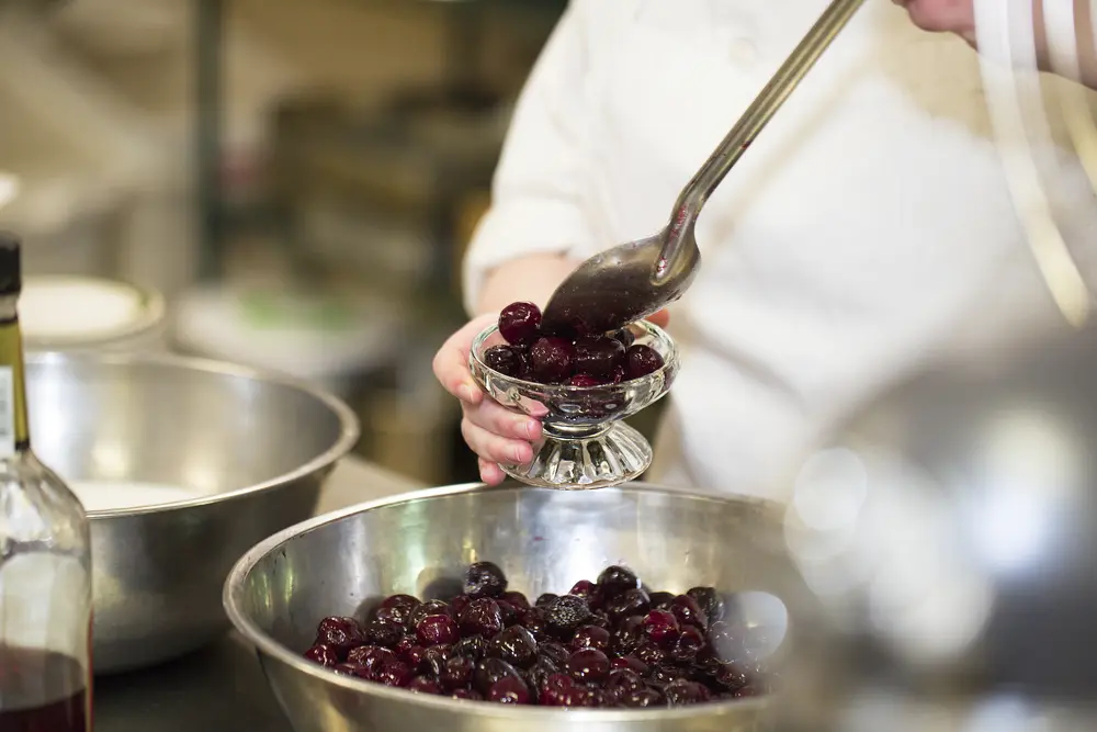 Culinary students placing cherries into a glass dish in a kitchen.