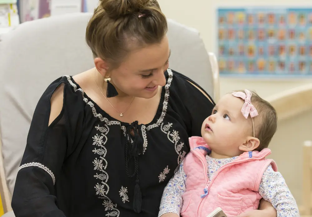 Early Childhood Education student holding a baby in a rocking chair, smiling.
