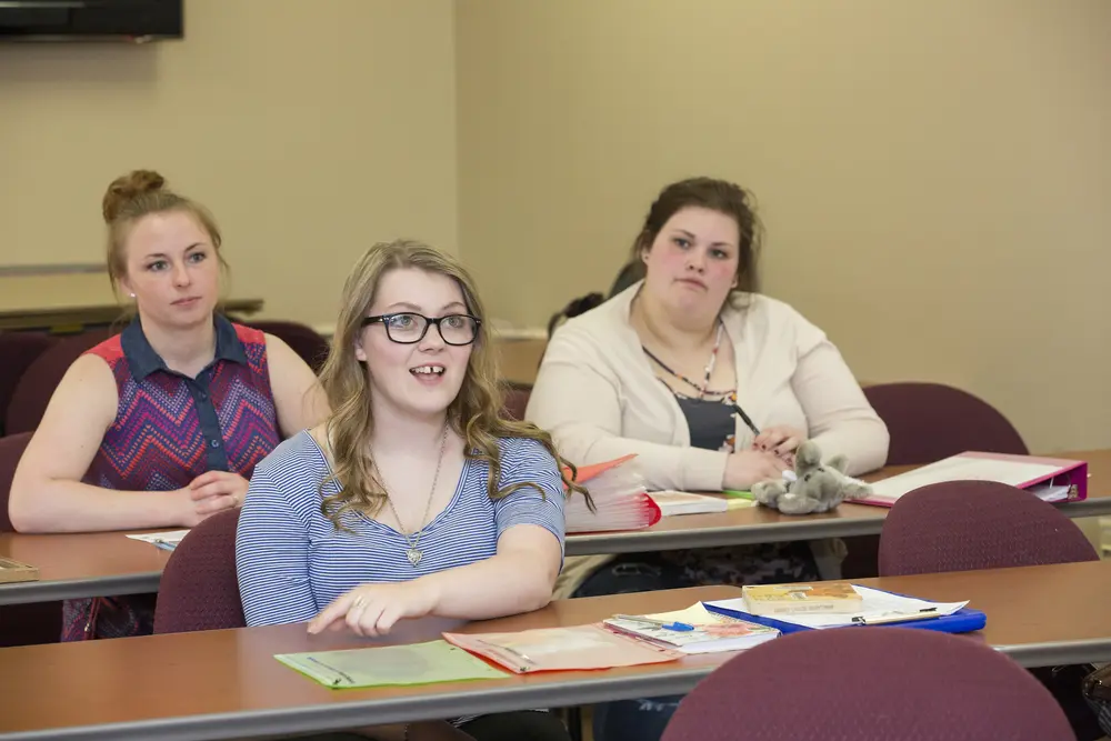 Three Early Childhood Education students seated at desks, engaged in a classroom setting.