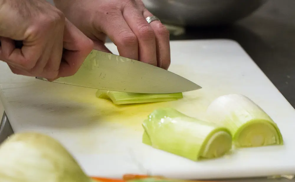 Slicing leeks on a white cutting board with a large knife.