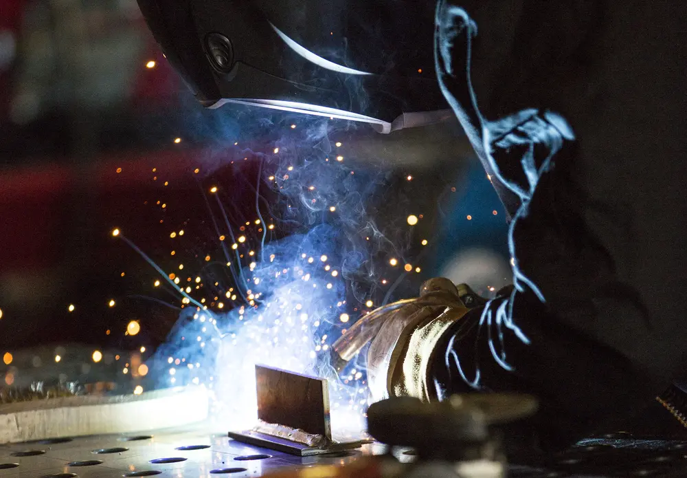 Welder in action with sparks flying, wearing protective gear.