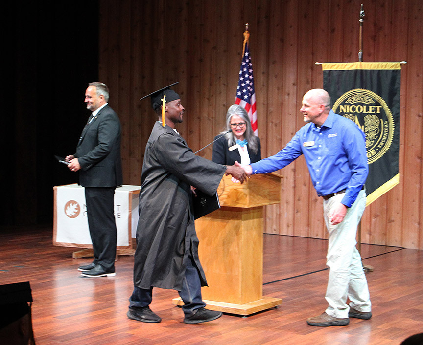 graduate walks across stage and shakes hand with instructor