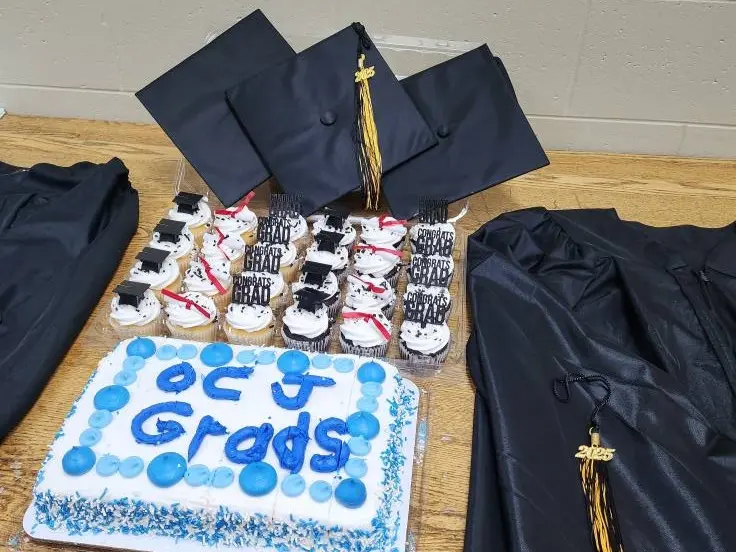 Graduation caps, gowns, cupcakes and cake displayed on a table.