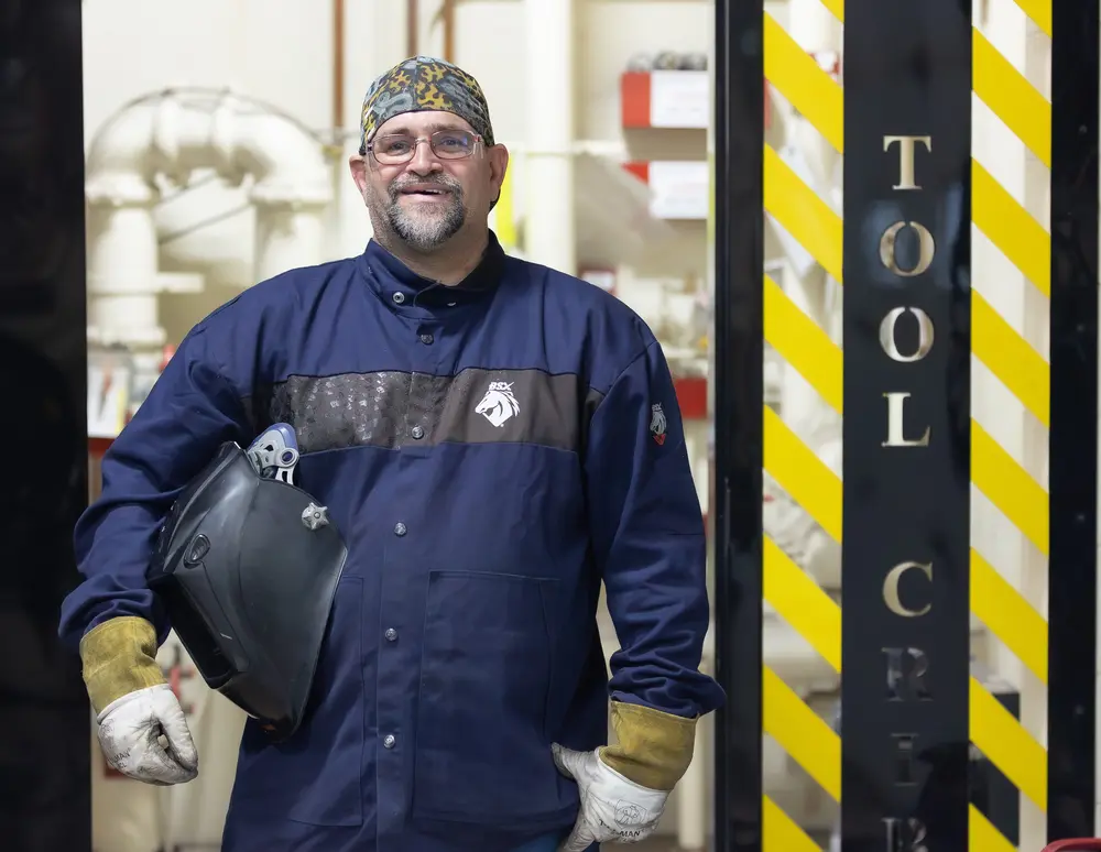 Welder in protective gear standing in front of a tool cart.