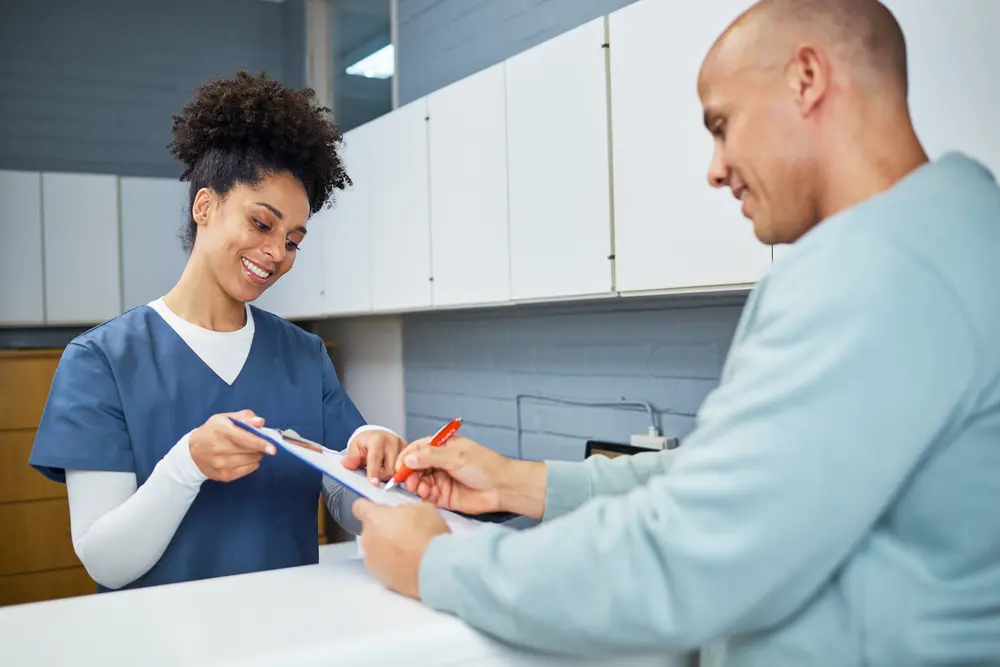 Nurse assisting man with medical form at a counter.