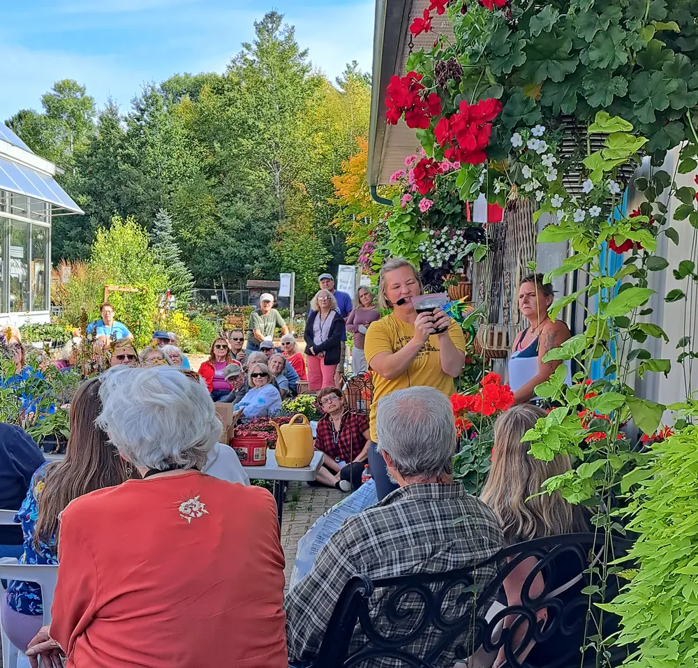 People gathered outdoors near a greenhouse, surrounded by colorful flowers.