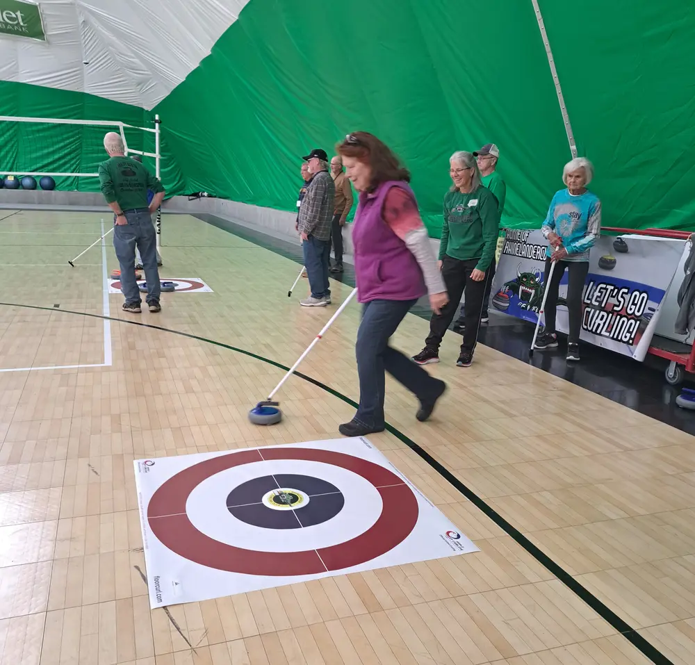 Players enjoy indoor curling on a wooden court.