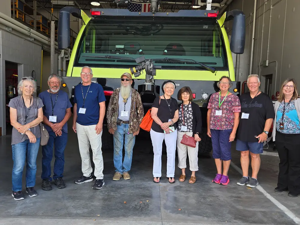 Group of senior citizens posing in a line in front of a large airport truck.