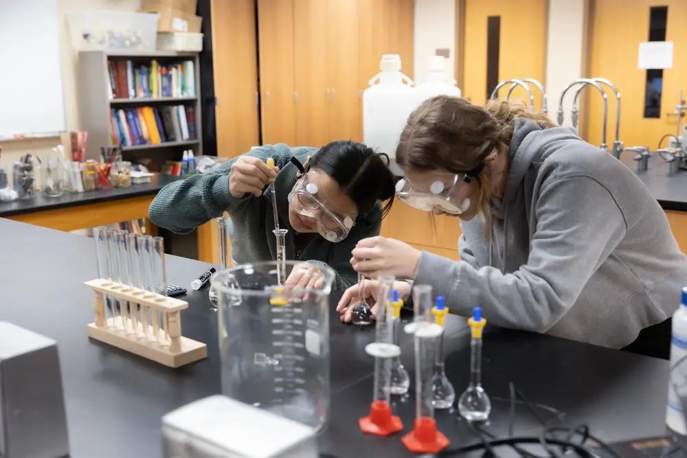 Students working on a science experiment in a lab with test tubes and safety goggles.